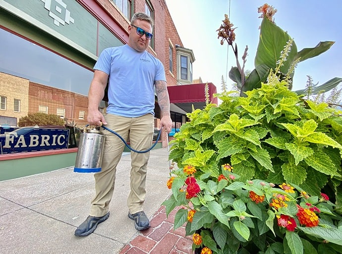 A man with a watering can in front of a flower pot.