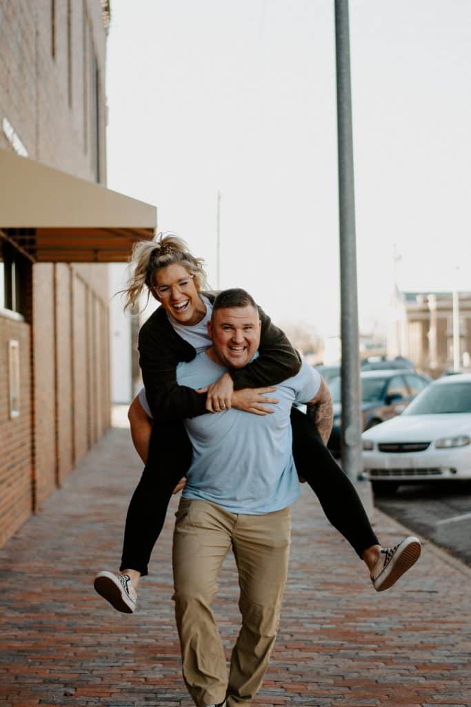 A man is being carried by a woman on a brick sidewalk.