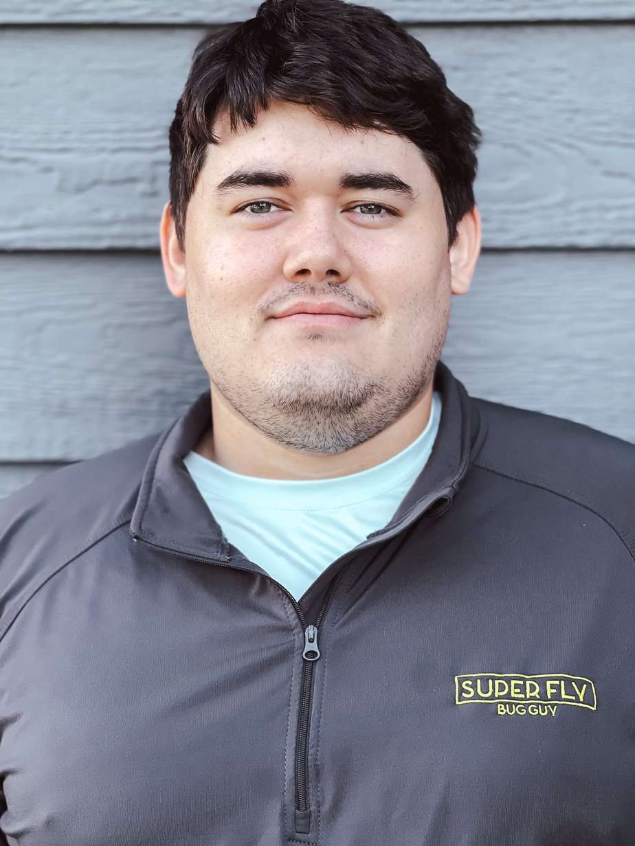 A young man in a gray jacket is standing in front of a gray wall.